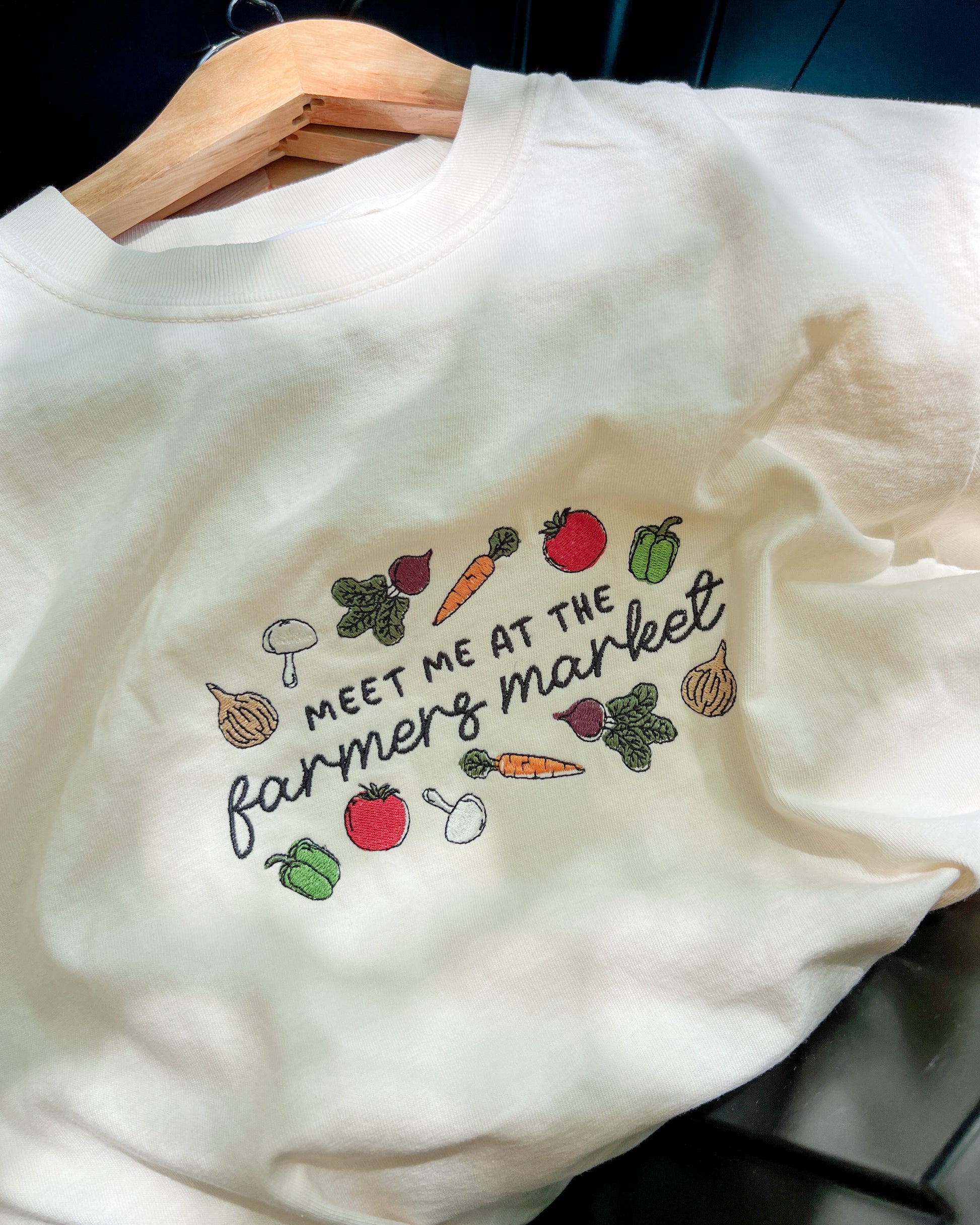 White sweatshirt with colorful vegetable graphics and text on a hanger.