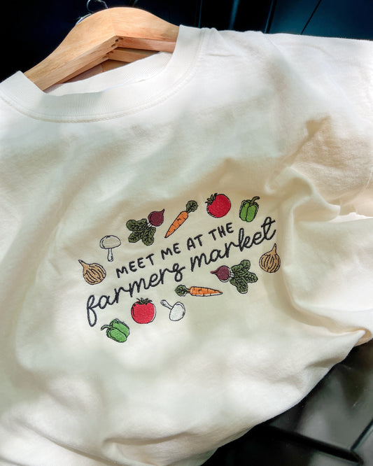 White sweatshirt with colorful vegetable graphics and text on a hanger.